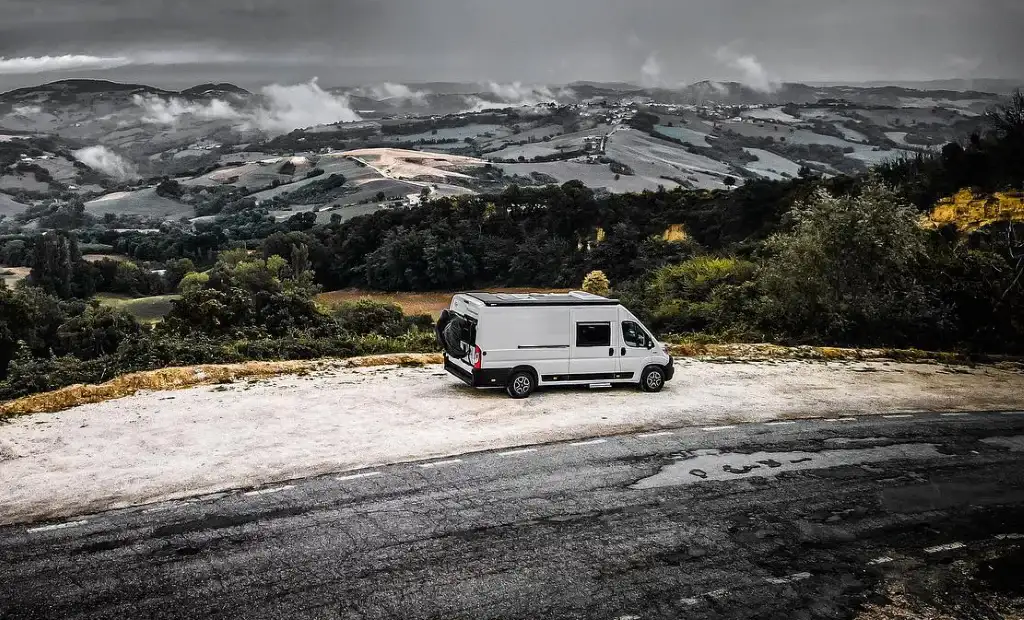 Fourgon aménagé blanc sur plaine à flanc de collines avec vue à 360 degrés